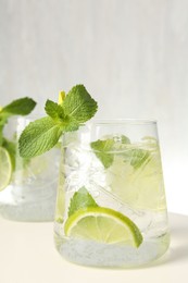 Photo of Tasty cocktail with lime and ice cubes on white table, closeup