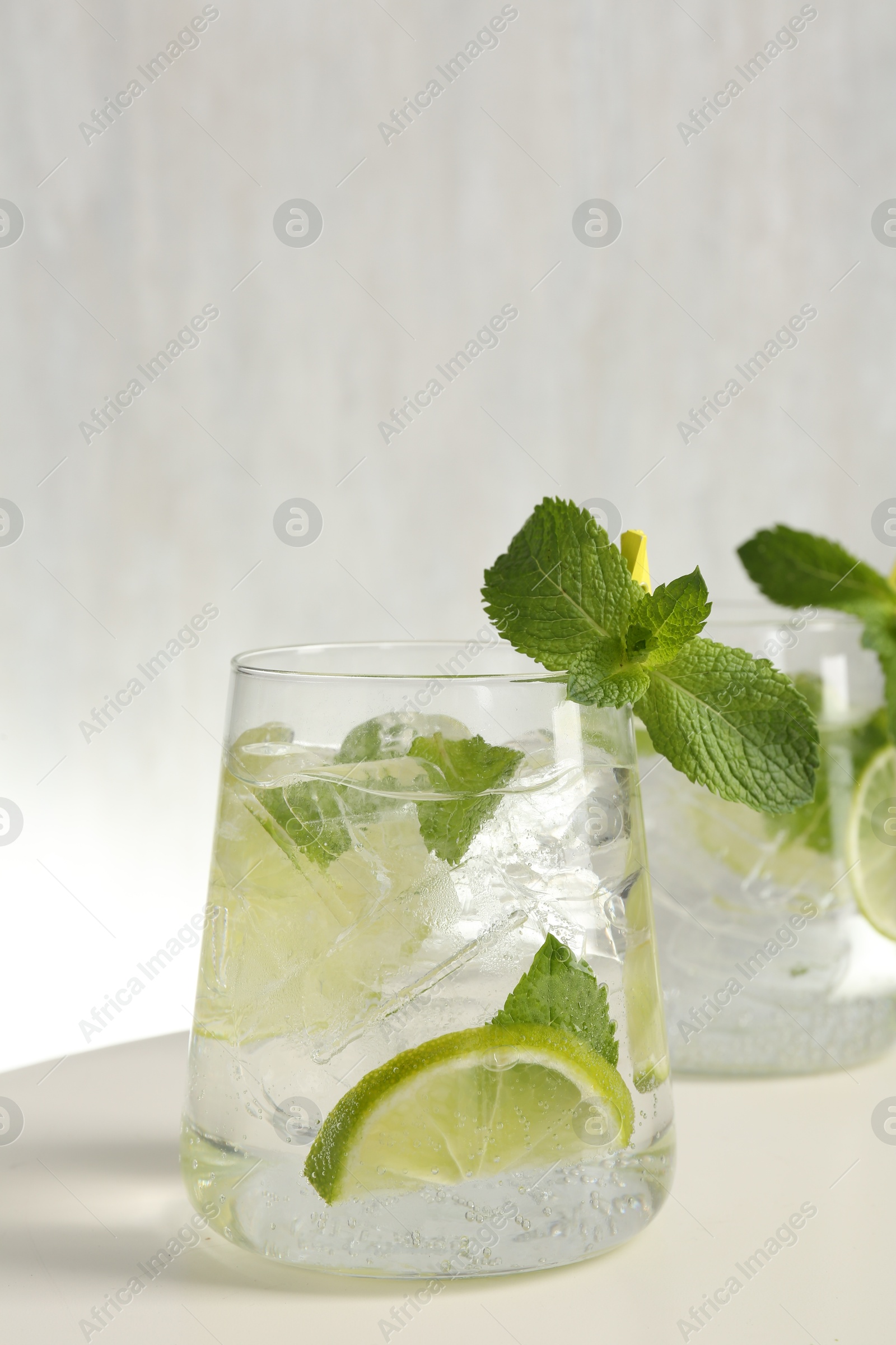 Tasty cocktail with lime and ice cubes on white table, closeup Photo of Tasty cocktail with lime and ice cubes on white table, closeup