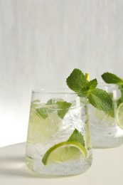 Photo of Tasty cocktail with lime and ice cubes on white table, closeup