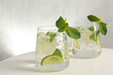 Photo of Tasty cocktail with lime and ice cubes on white table, closeup