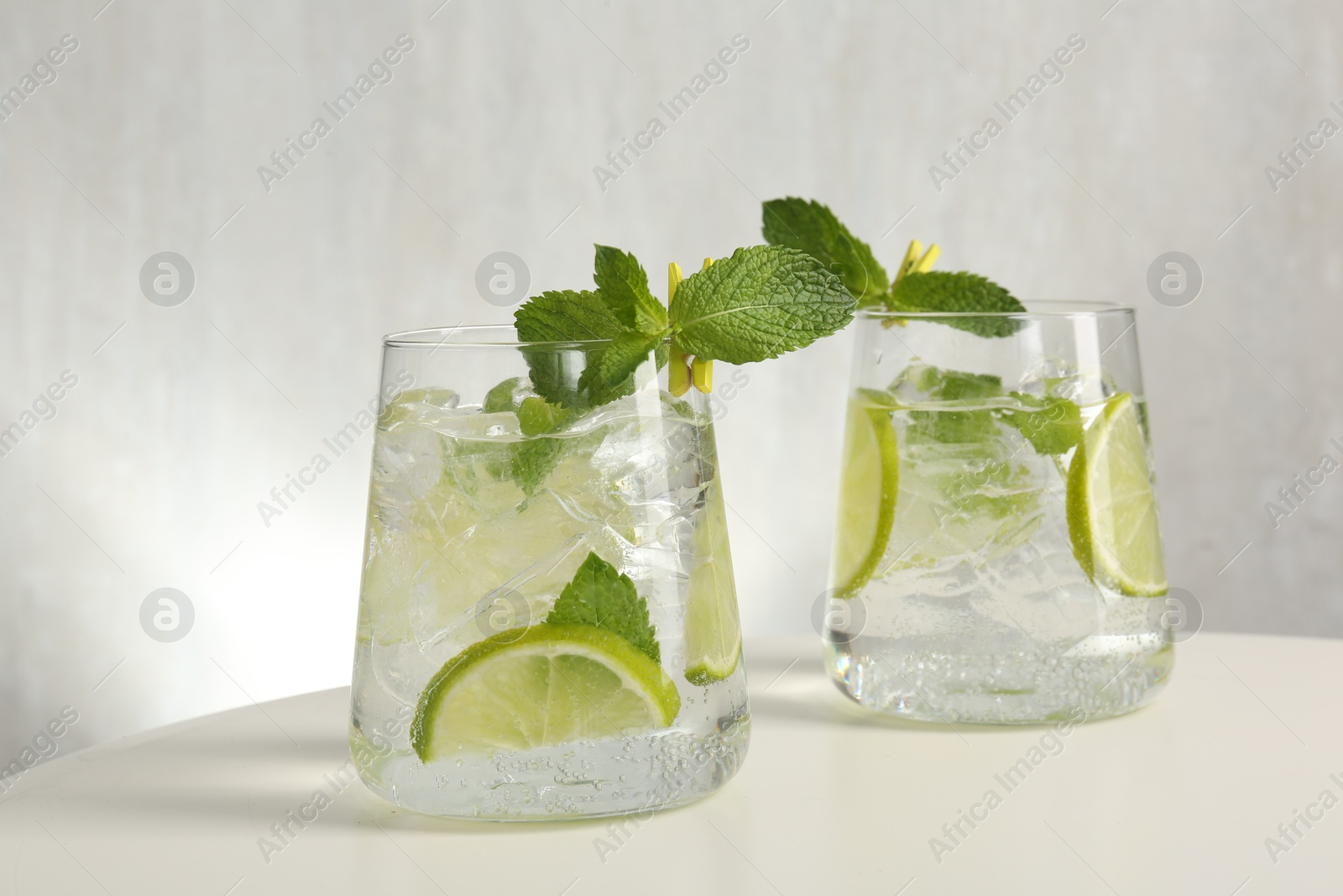 Tasty cocktail with lime and ice cubes on white table, closeup Photo of Tasty cocktail with lime and ice cubes on white table, closeup