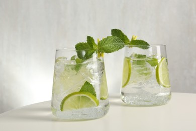 Photo of Tasty cocktail with lime and ice cubes on white table, closeup
