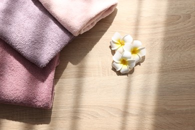 Photo of Soft towels and plumeria flowers on wooden table, flat lay