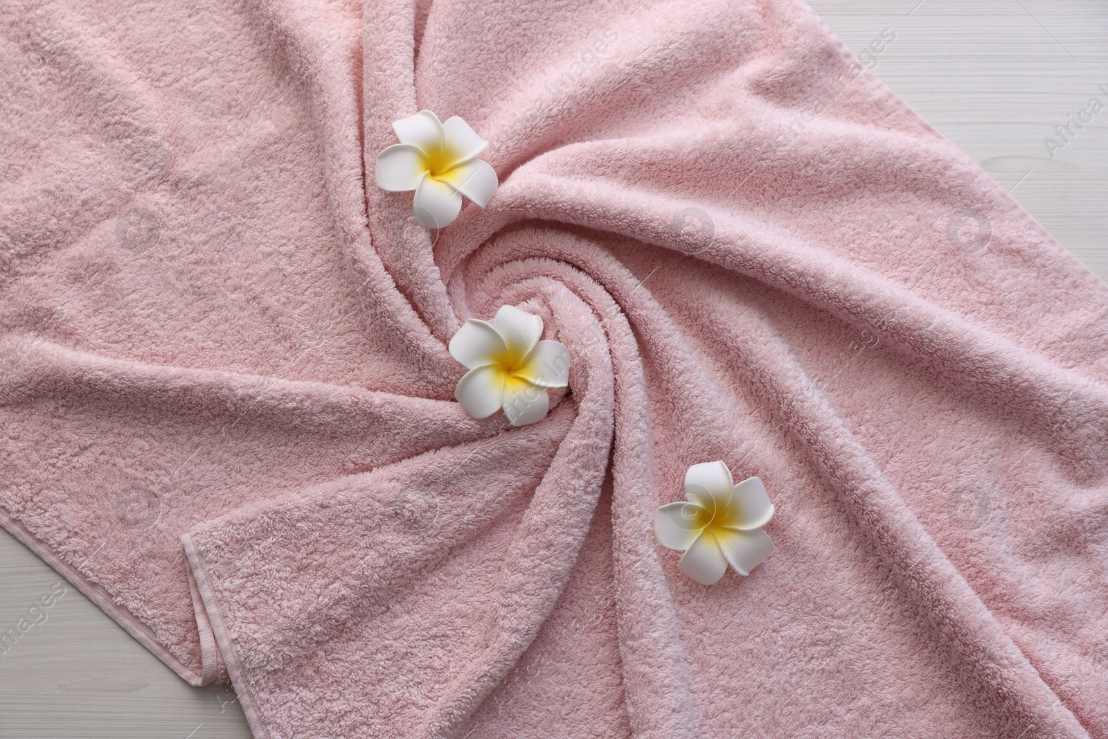 Photo of Pink towel and plumeria flowers on light wooden table, top view