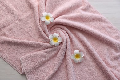 Photo of Pink towel and plumeria flowers on light wooden table, top view