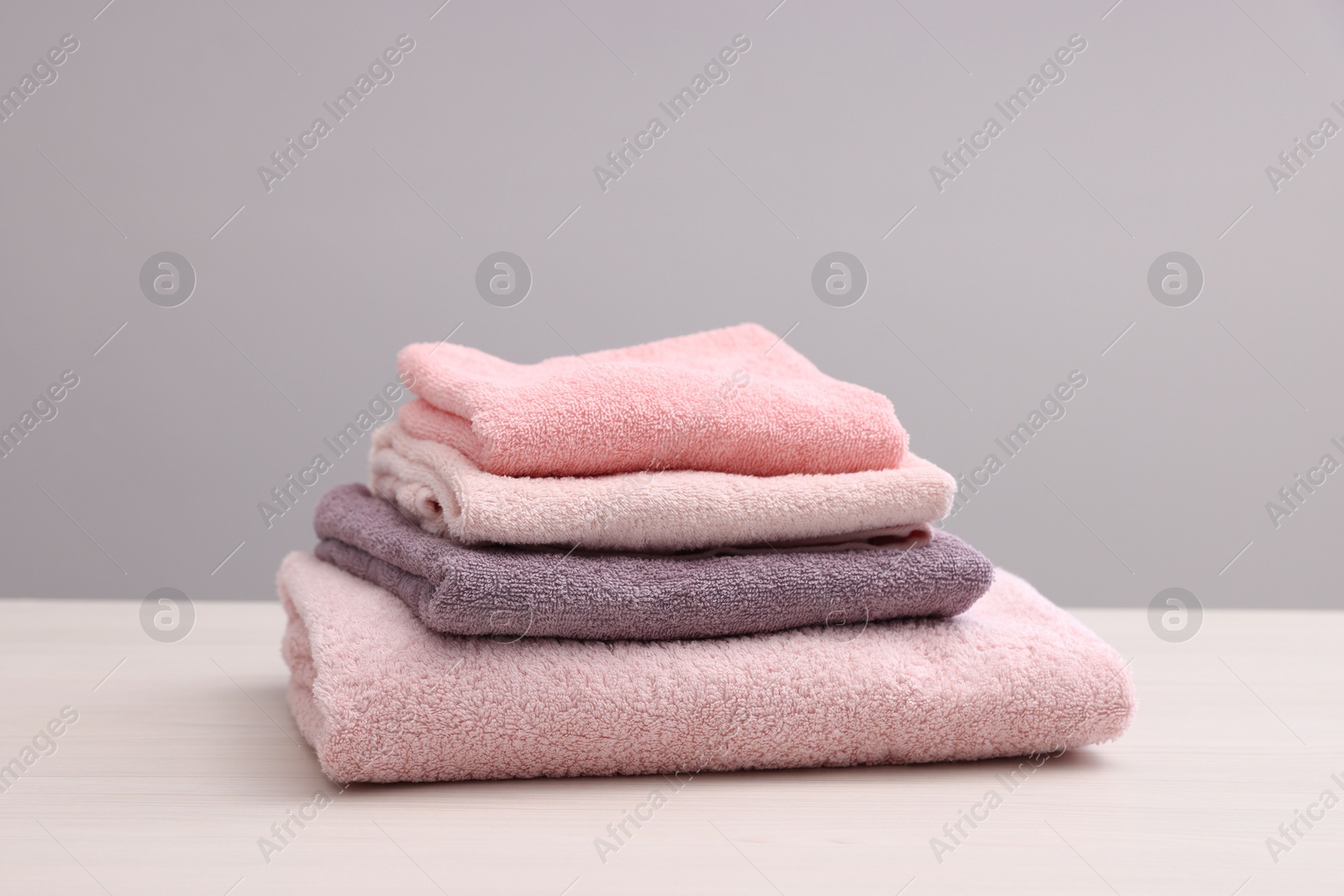 Photo of Stack of soft towels on light wooden table against grey background, closeup