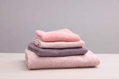 Photo of Stack of soft towels on light wooden table against grey background, closeup