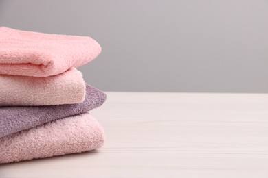 Photo of Stack of soft towels on light wooden table against grey background, closeup. Space for text