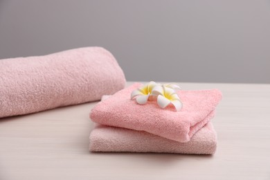 Photo of Pink towels and plumeria flowers on light wooden table against grey background, closeup