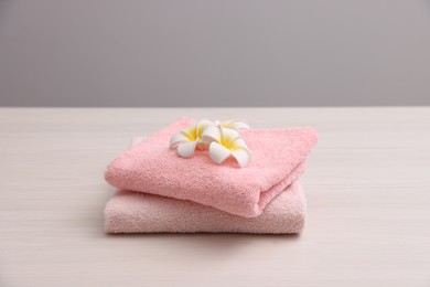 Photo of Pink towels and plumeria flowers on light wooden table against grey background, closeup