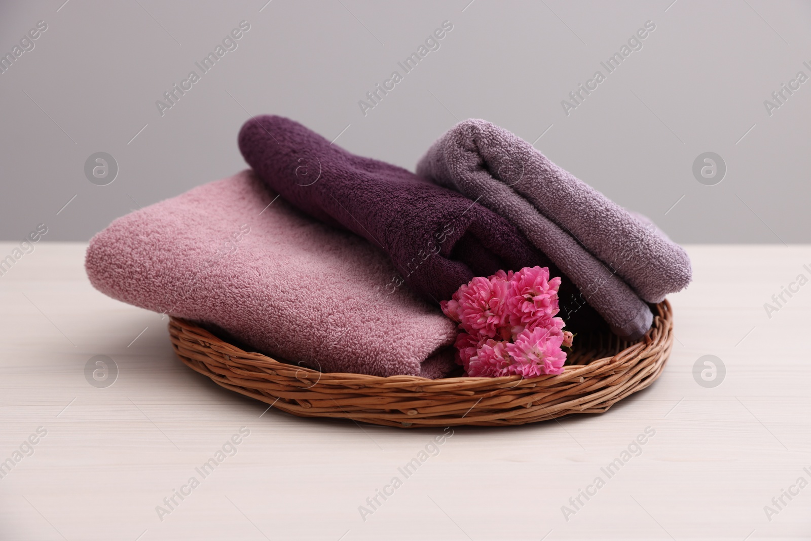 Photo of Soft towels and flowers on light wooden table against grey background, closeup