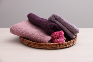 Photo of Soft towels and flowers on light wooden table against grey background, closeup
