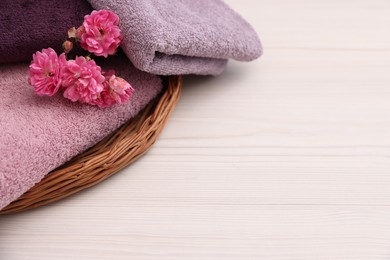 Photo of Soft towels and flowers on light wooden table, closeup. Space for text