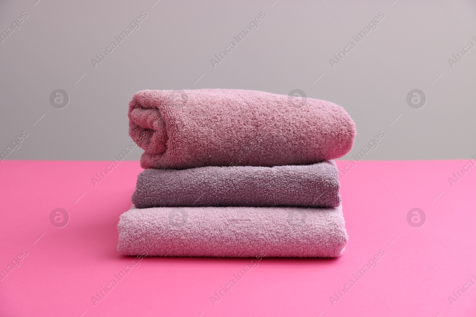 Photo of Stack of soft towels on pink table against grey background, closeup