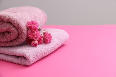 Photo of Soft towels and flowers on pink table against grey background, closeup. Space for text