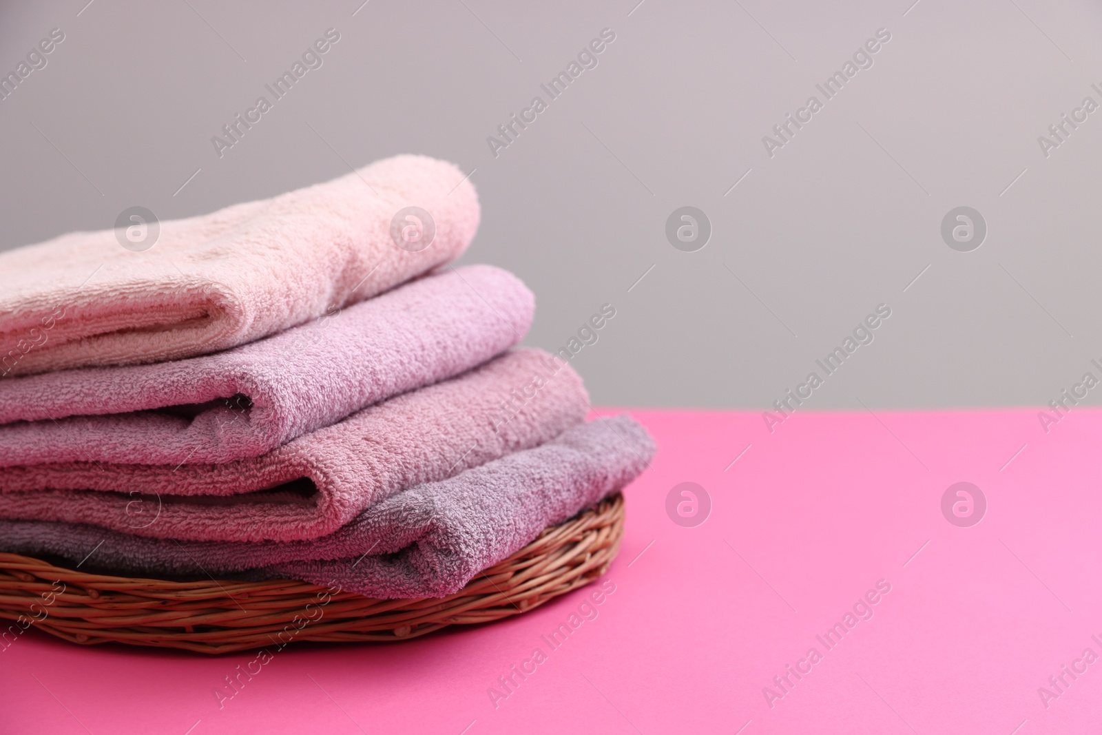 Photo of Stack of soft towels on pink table against grey background, closeup. Space for text
