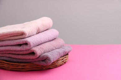 Photo of Stack of soft towels on pink table against grey background, closeup. Space for text