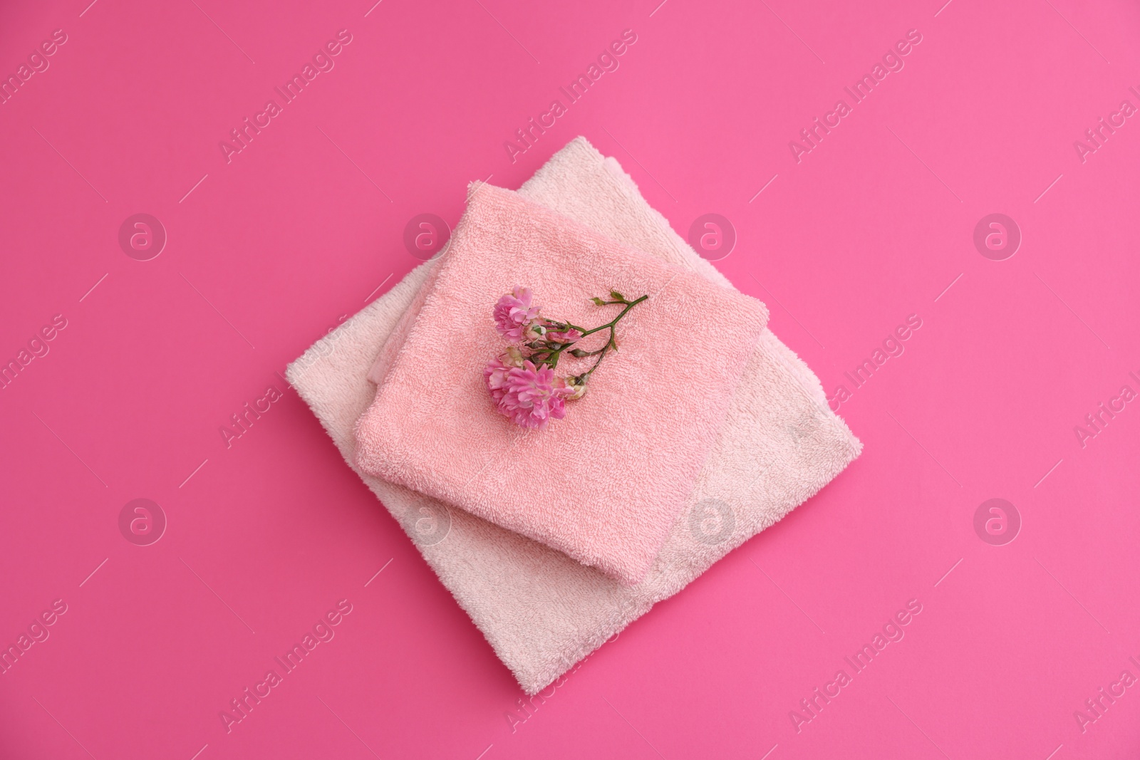 Photo of Soft towels and flowers on pink background, top view