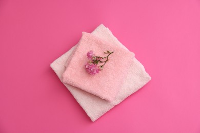 Photo of Soft towels and flowers on pink background, top view
