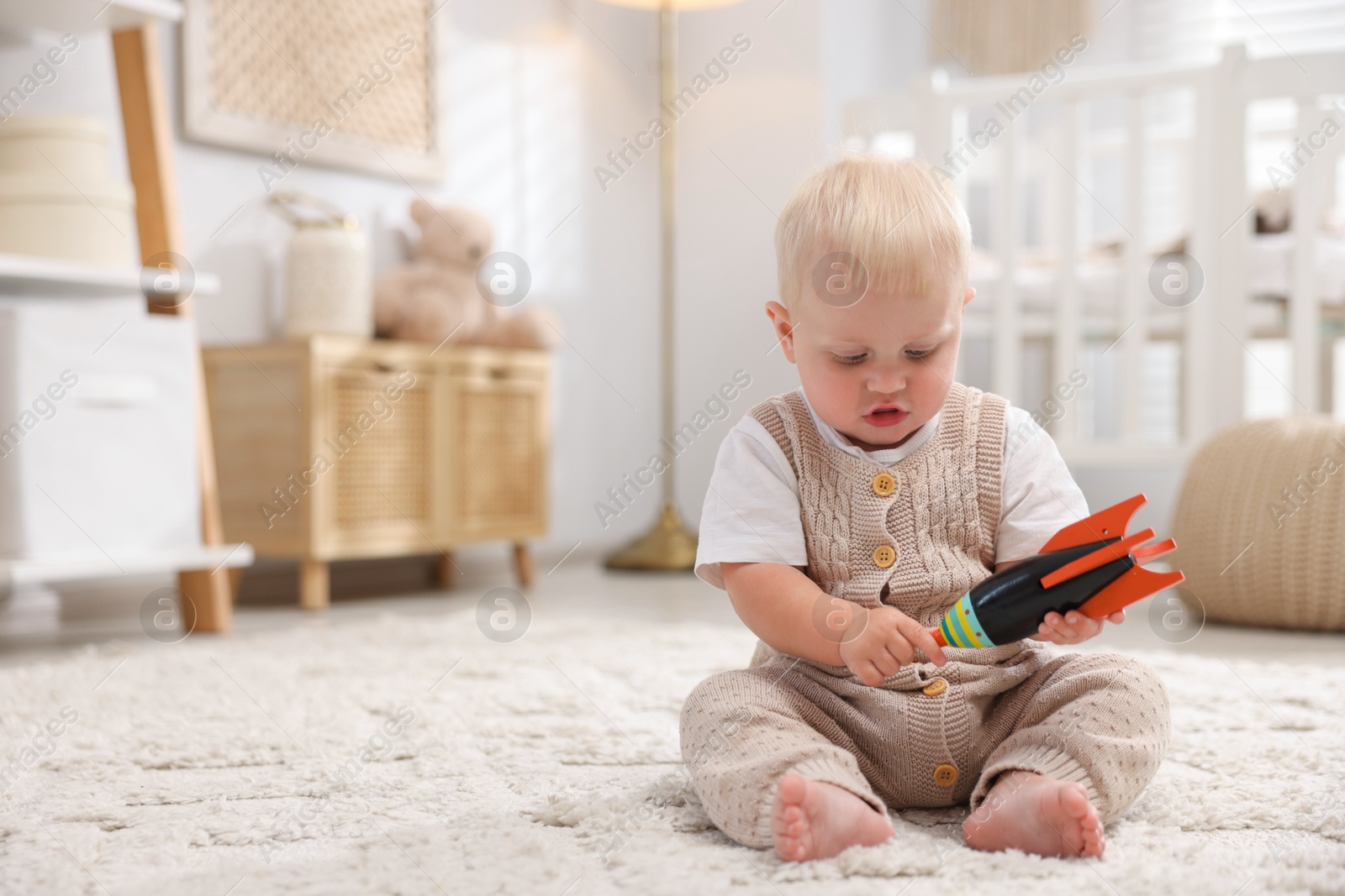 Photo of Cute newborn baby playing with toy in light room. Space for text