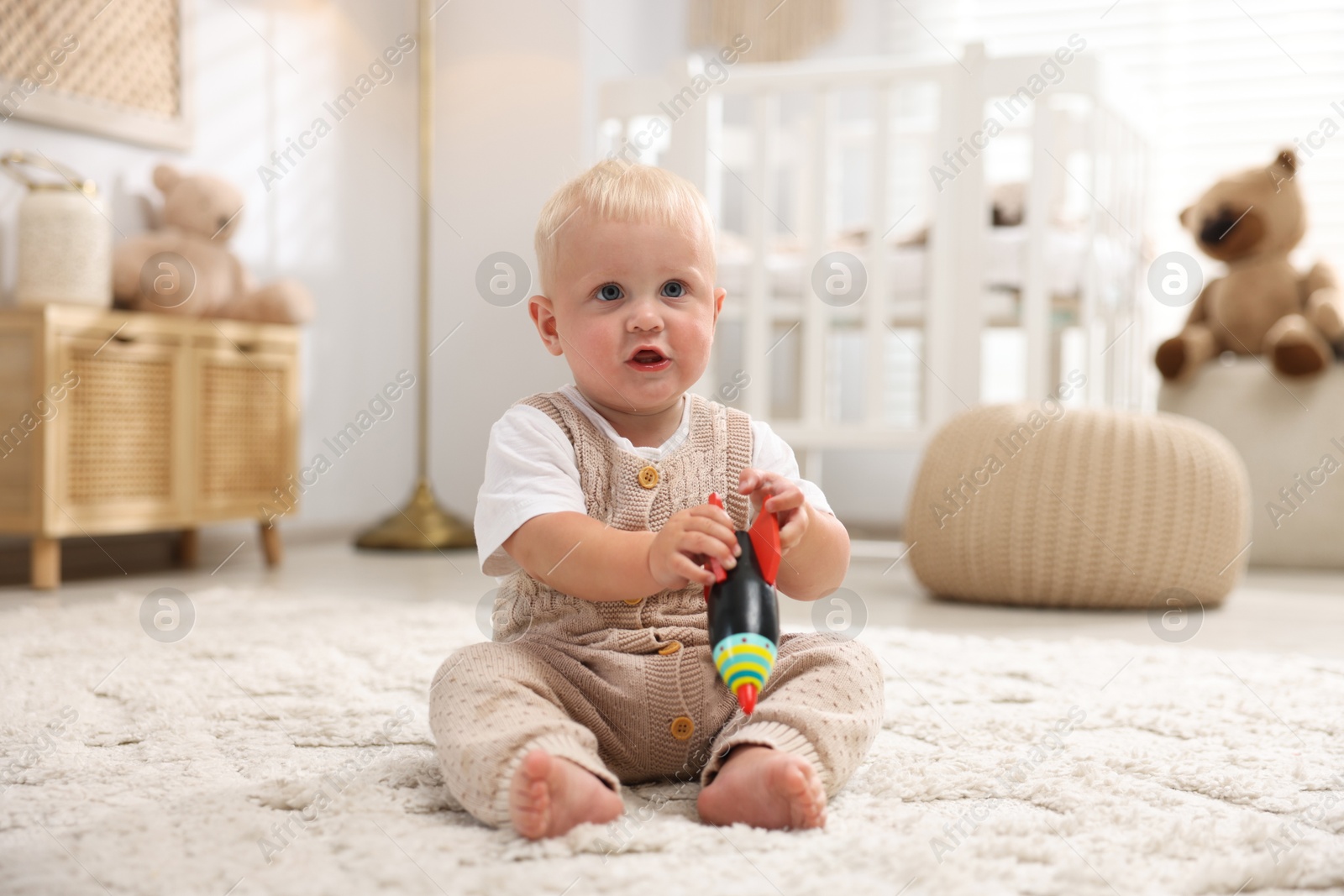 Photo of Cute newborn baby playing with toy on carpet in light room