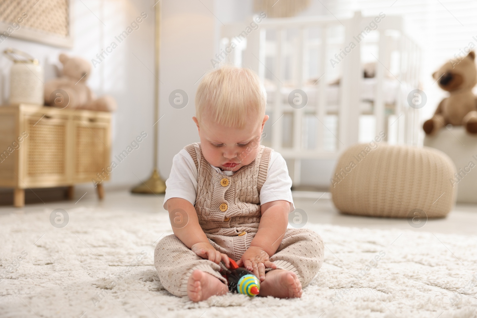 Photo of Cute newborn baby playing with toy on carpet in light room