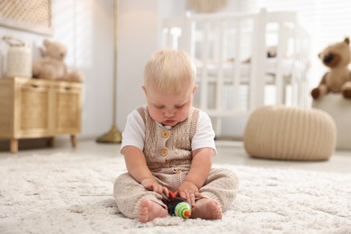 Photo of Cute newborn baby playing with toy on carpet in light room