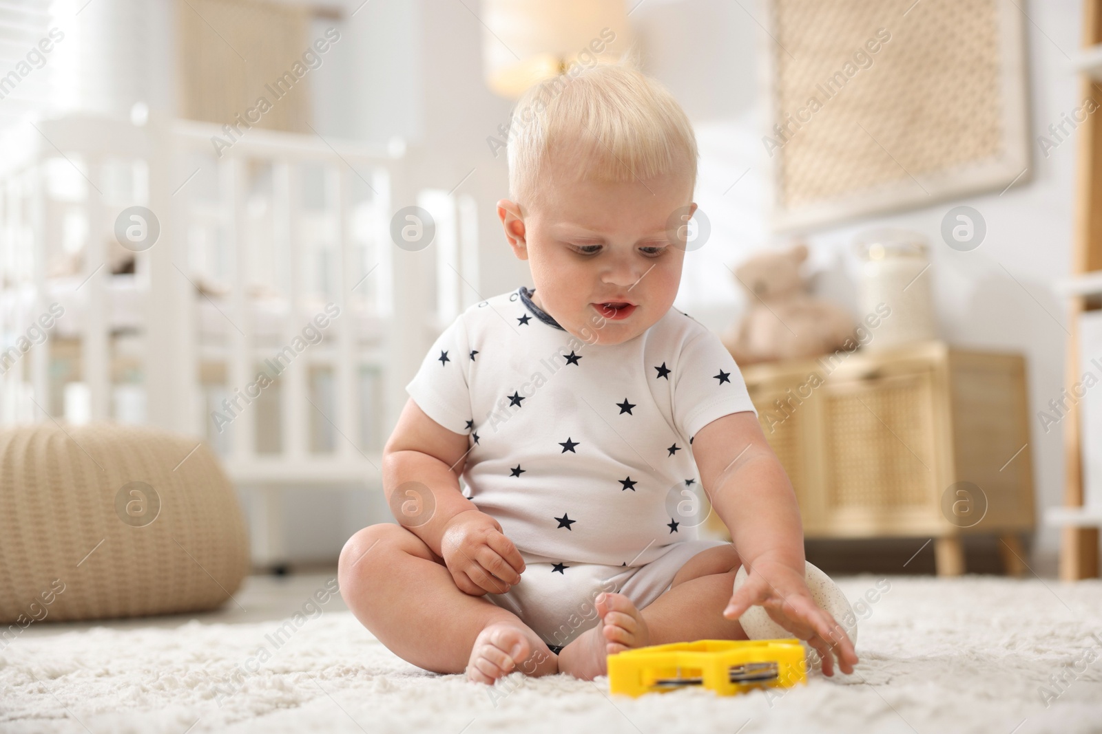 Photo of Cute newborn baby playing with toy on carpet in light room