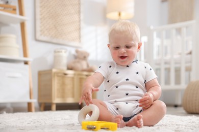 Photo of Cute newborn baby playing with toys on carpet in light room. Space for text