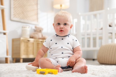 Photo of Cute newborn baby with toys on carpet in light room