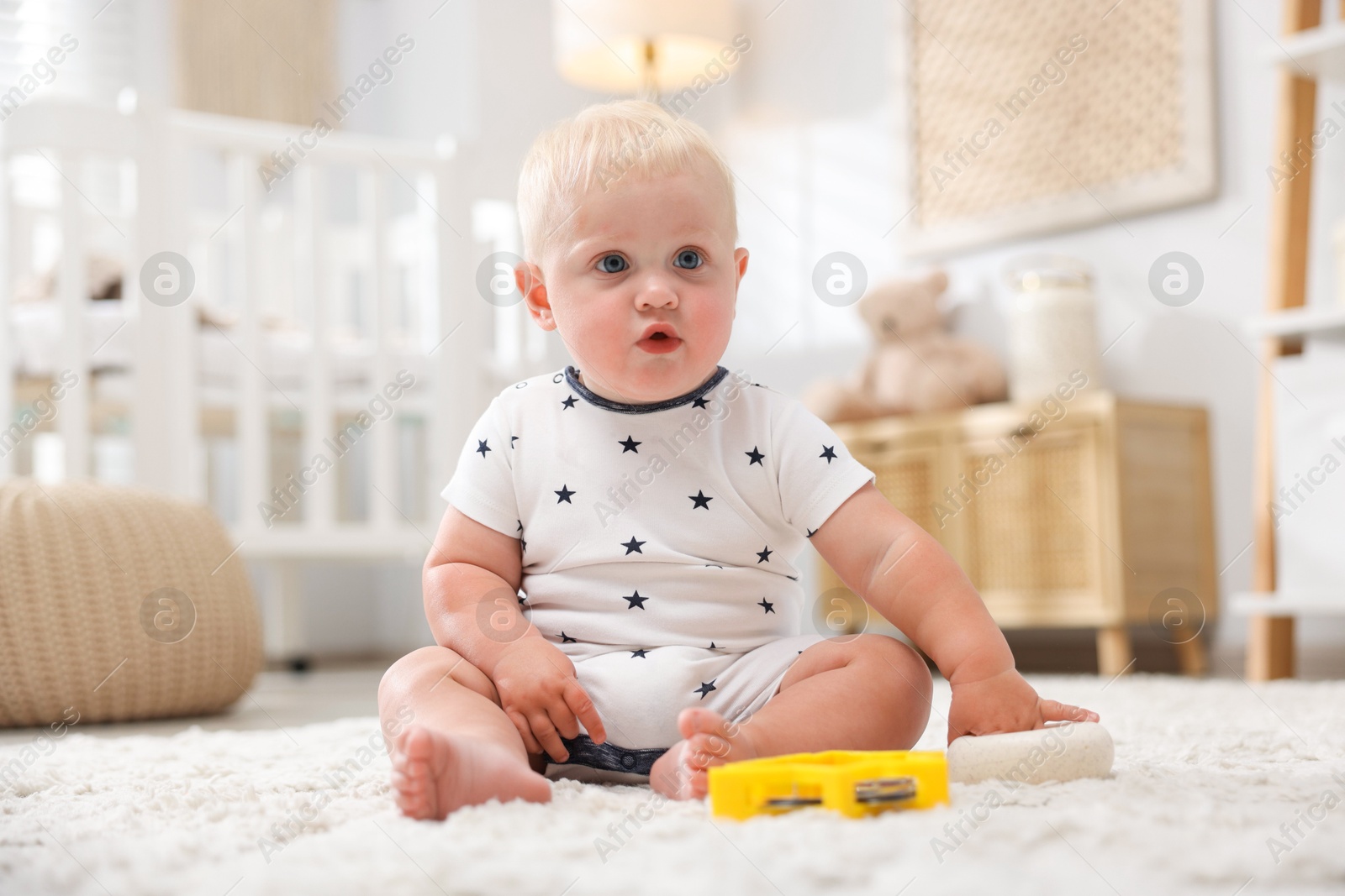 Photo of Cute newborn baby with toys on carpet in light room