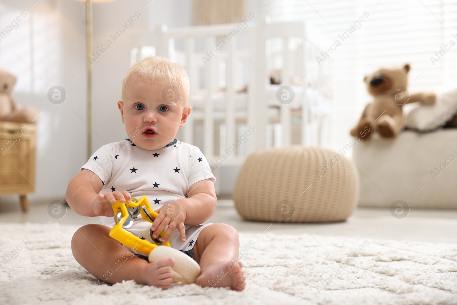 Photo of Cute newborn baby playing with toy tambourine on carpet in light room. Space for text