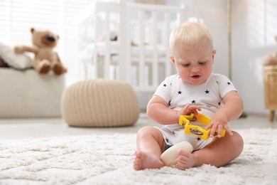 Photo of Cute newborn baby playing with toy tambourine on carpet in light room. Space for text