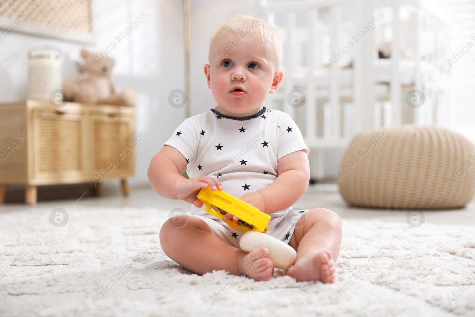 Photo of Cute newborn baby playing with toy on carpet in light room