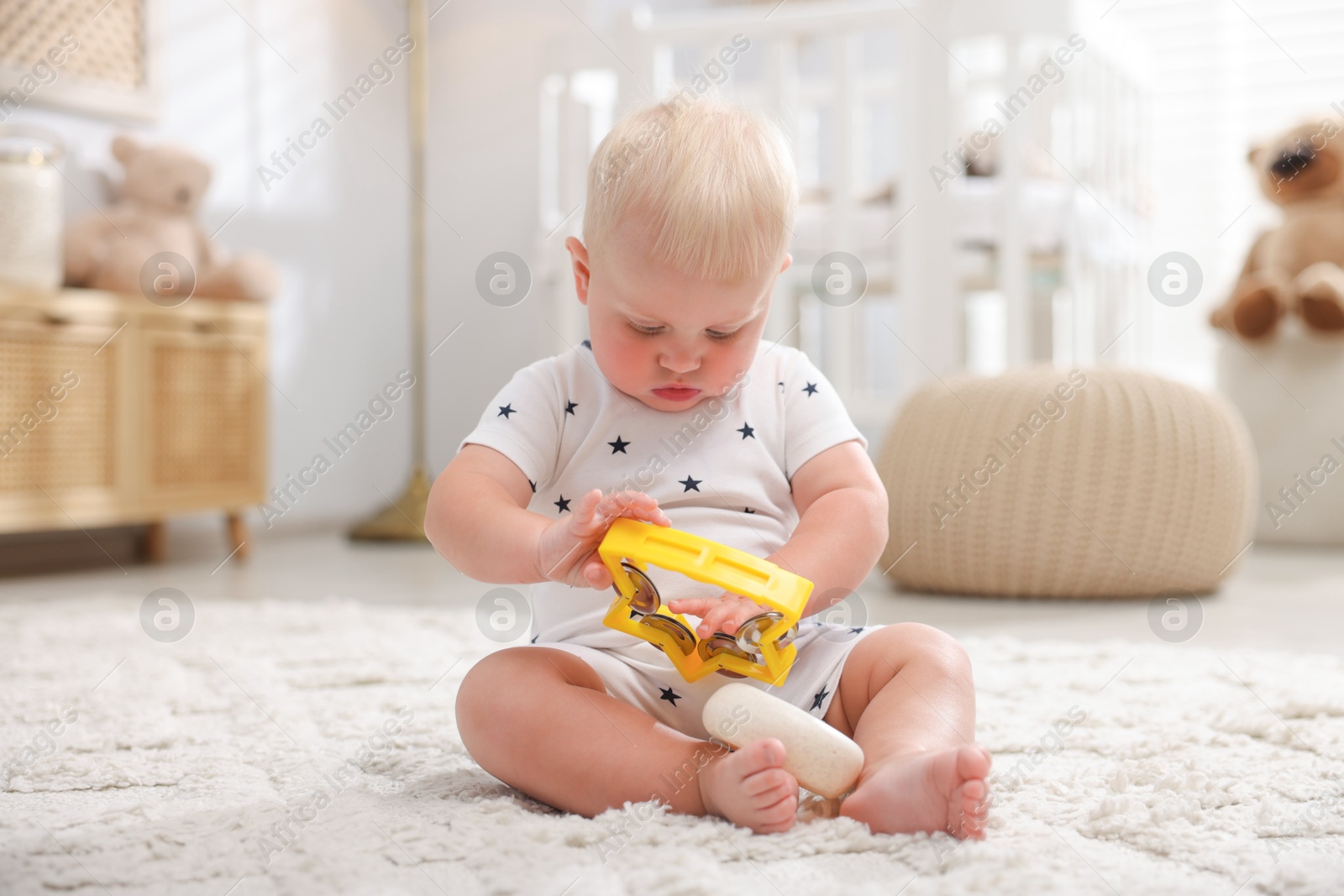 Photo of Cute newborn baby playing with toy on carpet in light room