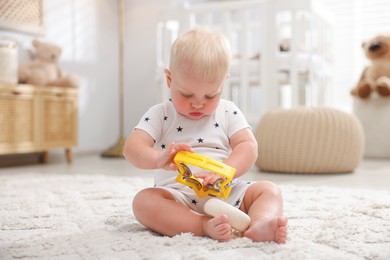 Photo of Cute newborn baby playing with toy on carpet in light room