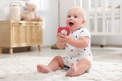 Photo of Cute newborn baby playing with toy on carpet in light room
