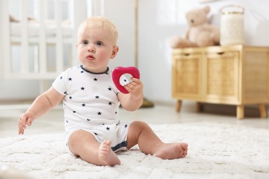 Photo of Cute newborn baby playing with toy on carpet in light room