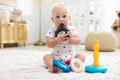 Photo of Cute newborn baby playing with toy on carpet in light room