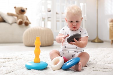 Photo of Cute newborn baby playing with toy on carpet in light room