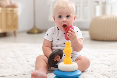 Photo of Cute newborn baby playing with toy on carpet in light room