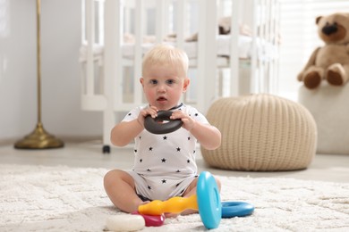 Photo of Cute newborn baby playing with toy on carpet in light room