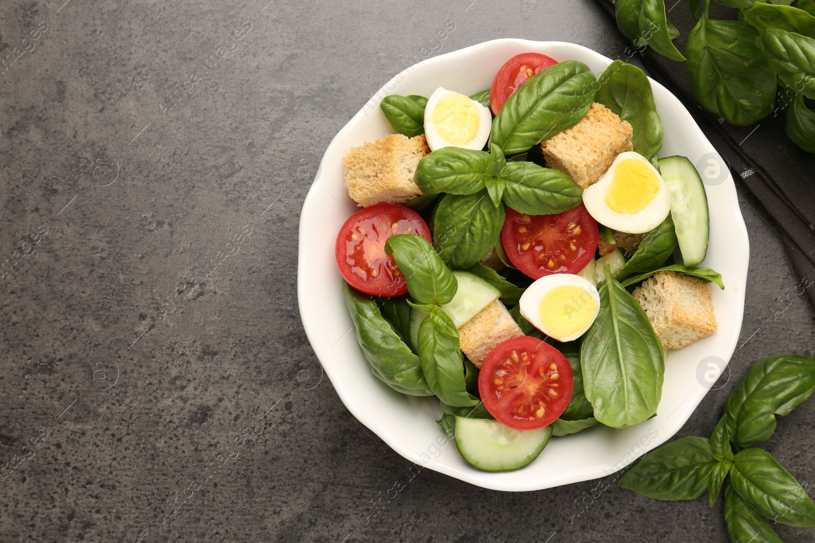 Photo of Tasty salad with croutons, tomatoes, cucumbers and basil on black table, flat lay. Space for text