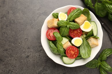 Photo of Tasty salad with croutons, tomatoes, cucumbers and basil on black table, flat lay. Space for text