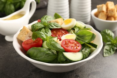 Photo of Tasty salad with croutons, tomatoes, cucumbers and basil on black table, closeup