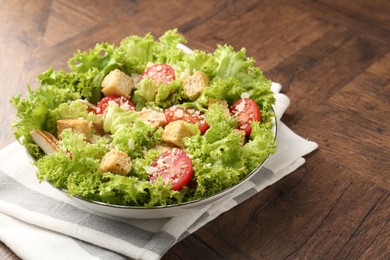 Photo of Tasty salad with croutons, tomatoes, cheese and chicken on wooden table, closeup