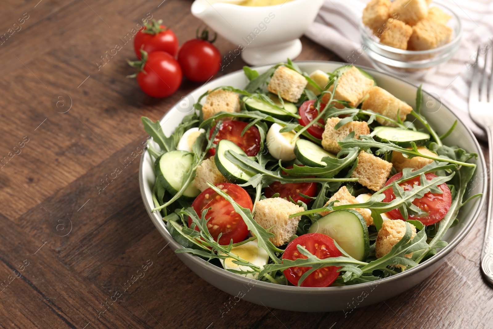 Photo of Tasty salad with croutons, cucumbers, tomatoes and arugula on wooden table, closeup. Space for text