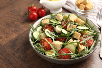 Photo of Tasty salad with croutons, cucumbers, tomatoes and arugula on wooden table, closeup. Space for text