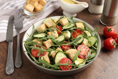 Photo of Tasty salad with croutons, cucumbers, tomatoes and arugula on wooden table, closeup