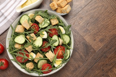 Photo of Tasty salad with croutons, cucumbers, tomatoes and arugula on wooden table, flat lay. Space for text